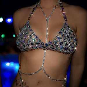 May include: A silver body chain with iridescent rhinestones. The chain is worn as a bra and a belt.