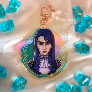 May include: A holographic acrylic keychain featuring a character with blue hair and a stern expression. The character wears a blue and white outfit with gold accents. The keychain has a star-shaped clasp and is surrounded by blue crystal-like decorations.