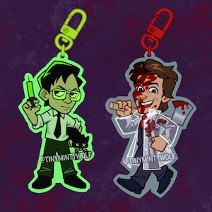 May include: Two cartoon-style keychains. One features a green-skinned character with glasses holding a syringe. The other depicts a character covered in blood, holding an axe. Both have a metal clasp.