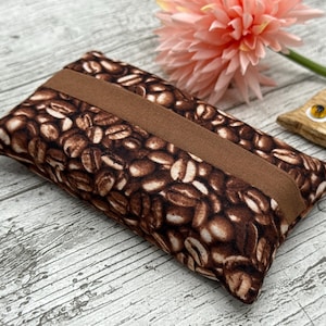 May include: A rectangular tissue box cover featuring a coffee bean design in brown and tan hues. A solid brown band is across the centre. A pink flower and a wooden owl decoration are in the background.