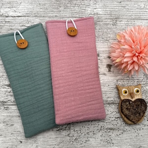 May include: Two rectangular fabric cases, one teal and one pink, each with a wooden button closure. A pink flower and a wooden owl decoration are also present. The cases are likely for a phone or glasses.