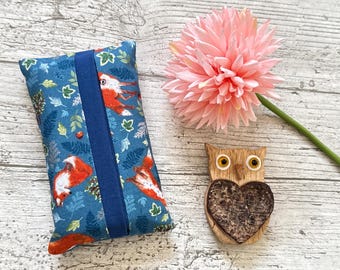 May include: A blue tissue box cover featuring a fox and leaf design, a pink flower, and a wooden owl figurine with a heart-shaped centre. The tissue box cover has a dark blue stripe down the middle.
