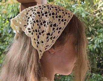 May include: Cream-colored, open-weave crochet headscarf. The head covering is triangular, with a delicate, lacy pattern. The headscarf is made of a soft, natural fiber, and is likely handmade. The head covering is a vintage style.