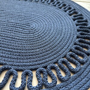 May include: A navy blue round braided rug with a decorative rope border. The rug has a woven texture and a circular shape.