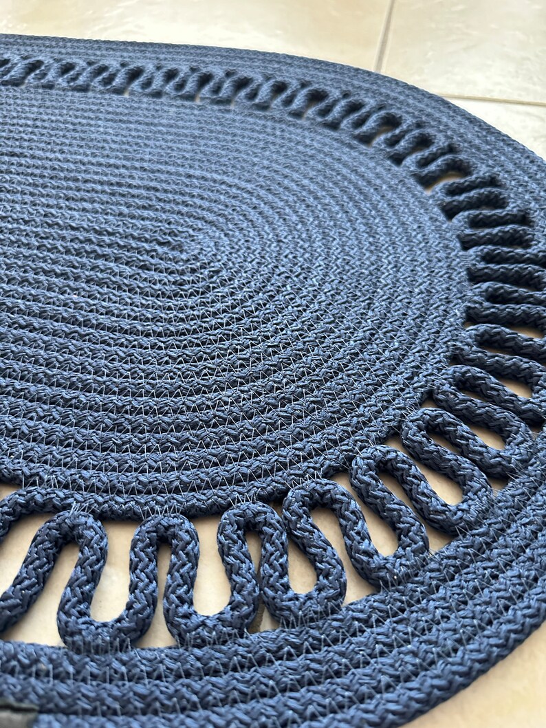 May include: A navy blue round braided rug with a decorative rope border. The rug has a woven texture and a circular shape.