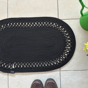 May include: Black oval braided rug with a decorative rope border. The rug is made of thick, woven rope and has a subtle texture.
