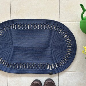 May include: A navy blue oval braided rug with a decorative border. The rug has a woven texture and a simple design.