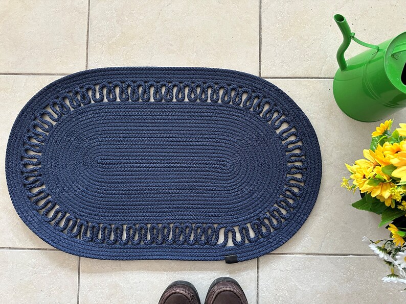 May include: A navy blue oval braided rug with a decorative border. The rug has a woven texture and a simple design.