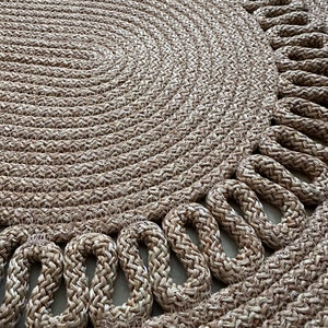 May include: A round, natural fiber rug with a woven design. The rug has a braided edge with a decorative pattern.