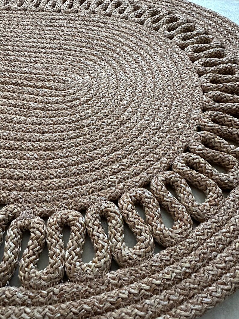 May include: A round, natural fiber rug with a woven design. The rug has a braided edge with a decorative pattern.
