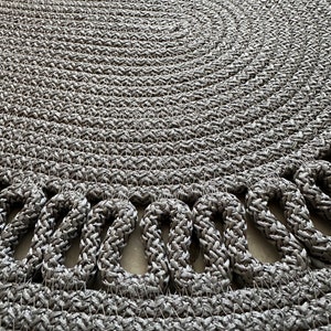 May include: A round, gray woven rug with a decorative border of looped strands.