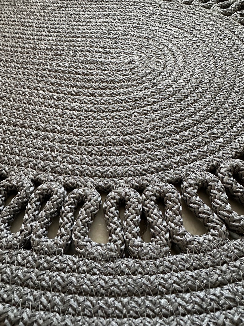 May include: A round, gray woven rug with a decorative border of looped strands.