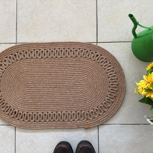 May include: A brown oval-shaped braided rug with a decorative border. The rug is made of natural fibers and has a rustic look.