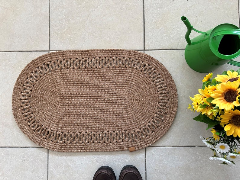 May include: A brown oval-shaped braided rug with a decorative border. The rug is made of natural fibers and has a rustic look.