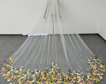 May include: A long white tulle wedding veil with a floral embroidery design in shades of yellow, pink, and green. The veil is shown on a white mannequin.