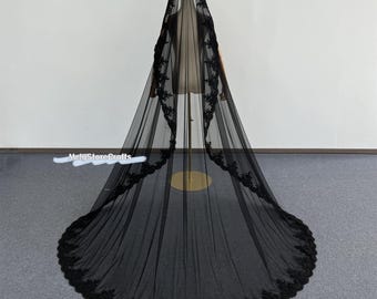 May include: A long, black bridal veil with a scalloped lace trim. The veil is made of a sheer fabric and is displayed on a mannequin. The lace trim is visible along the edges and around the bottom of the veil.