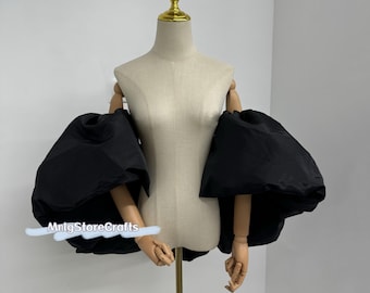 Könnte beinhalten: Ein schwarzes, übergroßes Ärmelkleidungsstück mit dramatischen, voluminösen Puffärmeln. Die Ärmel sind an einer Schaufensterpuppe mit Holzarmen und -händen befestigt. Die Schaufensterpuppe ist auf einem goldfarbenen Ständer montiert. Der Text "MnlgStoreCrafts" ist sichtbar.