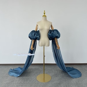 May include: A pair of long, blue, sheer sleeves with large, puffed shoulders. The sleeves are attached to a mannequin and are draped on the floor.