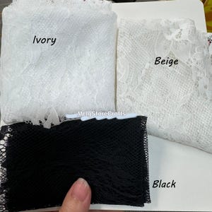May include: Close-up of three fabric swatches: ivory lace, beige lace, and black netting. The ivory and beige fabrics are folded, showcasing their delicate floral patterns. The black netting is a fine mesh. The word "Ivory", "Beige", and "Black" are written on the fabric.