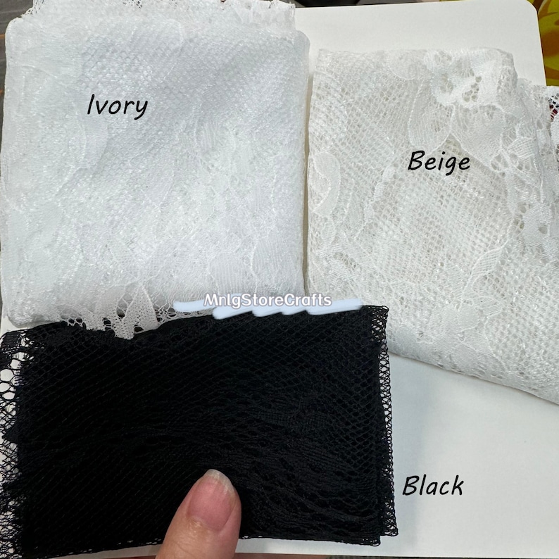 May include: Close-up of three fabric swatches: ivory lace, beige lace, and black netting. The ivory and beige fabrics are folded, showcasing their delicate floral patterns. The black netting is a fine mesh. The word "Ivory", "Beige", and "Black" are written on the fabric.