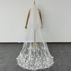 Peut inclure: Un voile de mariée blanc avec un motif de dentelle florale. Le voile est long et fluide, avec un délicat motif floral.