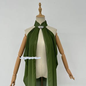 May include: A green chiffon cape with a silver leaf-shaped brooch. The cape is draped over a mannequin and has a high neckline.