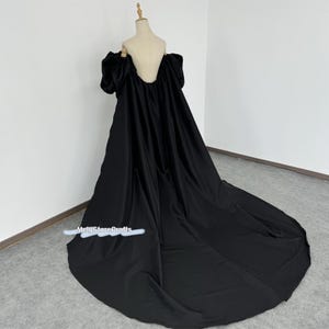 May include: A black off-the-shoulder gown with a long train and puffy sleeves. The gown is made of a smooth, silky fabric.