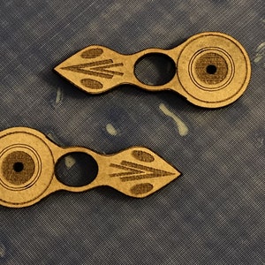 Puede incluir: Dos piezas decorativas de madera, de color marr&oacute;n claro, con un dise&ntilde;o circular y un peque&ntilde;o agujero en el centro. Cada pieza tiene un dise&ntilde;o geom&eacute;trico tallado en el mango.