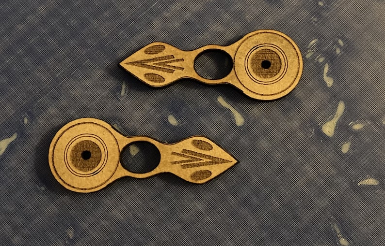 Puede incluir: Dos piezas decorativas de madera, de color marr&oacute;n claro, con un dise&ntilde;o circular y un peque&ntilde;o agujero en el centro. Cada pieza tiene un dise&ntilde;o geom&eacute;trico tallado en el mango.