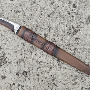 May include: A silver and brown dagger with a leather wrapped handle. The handle is wrapped with brown leather cord and has a silver metal cap at the end.