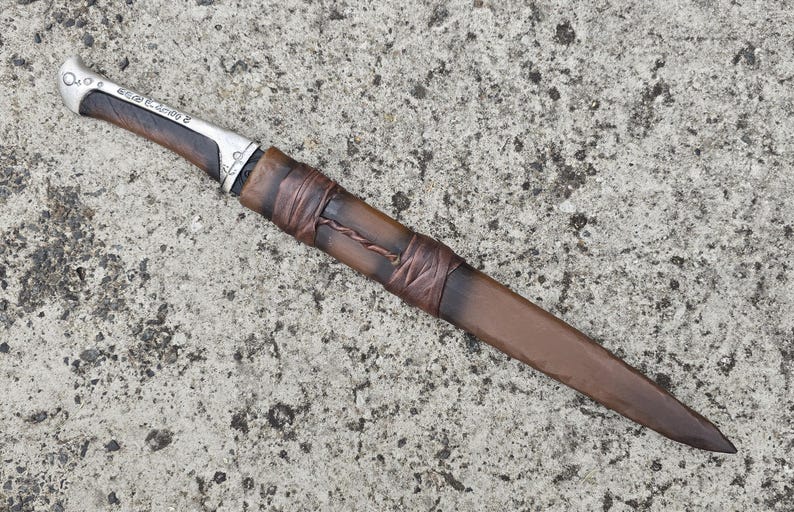 May include: A silver and brown dagger with a leather wrapped handle. The handle is wrapped with brown leather cord and has a silver metal cap at the end.