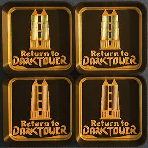 May include: Four gold-colored coasters with a black background. Each coaster features a stylized image of a tall building with the text "Return to DARK TOWER" in gold lettering.