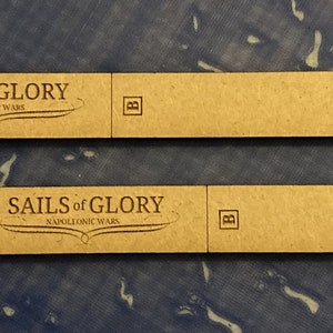 Puede incluir: Dos piezas de juego de madera marr&oacute;n para el juego de mesa "Sails of Glory: Napoleonic Wars". Cada pieza tiene una peque&ntilde;a "A" en el lado izquierdo, una "B" en el lado derecho y una serie de s&iacute;mbolos en el lado derecho.