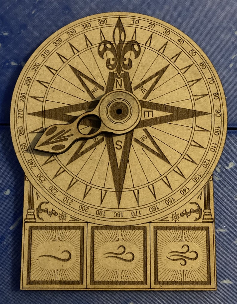 Puede incluir: Una br&uacute;jula de madera con un dise&ntilde;o de flor de lis en la parte superior y una flecha giratoria. La cara de la br&uacute;jula tiene n&uacute;meros del 0 al 360 grados y las direcciones cardinales est&aacute;n marcadas. La br&uacute;jula est&aacute; sobre una base de madera con tres cuadrados decorativos.