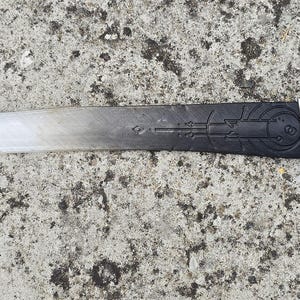 May include: A silver and black dagger with a wooden handle. The blade has a decorative pattern and the handle has the text "S. MATTHIAS. A.D. 1538".