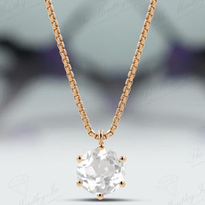 Pu&ograve; includere: Una collana color oro con una catena delicata e un grande pendente di pietra preziosa chiara e sfaccettata. Il pendente &egrave; a taglio brillante, che riflette la luce. Lo sfondo &egrave; sfocato, con sfumature di viola e bianco.