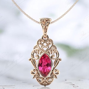 May include: A delicate gold pendant necklace with a pink marquise-shaped gemstone set in an intricate filigree design.