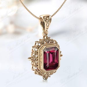 May include: A gold pendant necklace featuring an emerald-cut red gemstone set in a filigree frame.