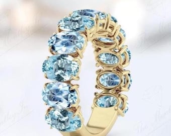 May include: A gold ring featuring a series of oval-cut, light blue gemstones. The gemstones are set closely together, creating a continuous band of color. The ring's band is a polished gold color.