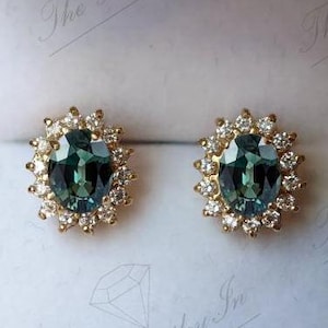 Può includere: Un paio di orecchini d'oro con una grande pietra preziosa verde di forma ovale circondata da un alone di diamanti più piccoli.