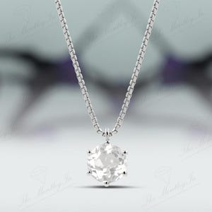Pu&ograve; includere: Una collana d'argento con un pendente esagonale in pietra preziosa trasparente. Il pendente &egrave; sospeso a una catena delicata. Lo sfondo sfocato ha sfumature di viola e bianco.
