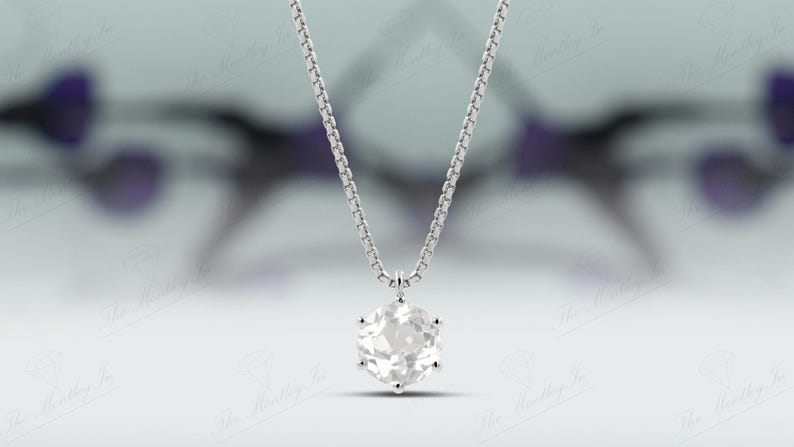Pu&ograve; includere: Una collana d'argento con un pendente esagonale in pietra preziosa trasparente. Il pendente &egrave; sospeso a una catena delicata. Lo sfondo sfocato ha sfumature di viola e bianco.
