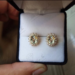 May include: A pair of gold earrings with oval-shaped green gemstones surrounded by a halo of smaller diamonds.