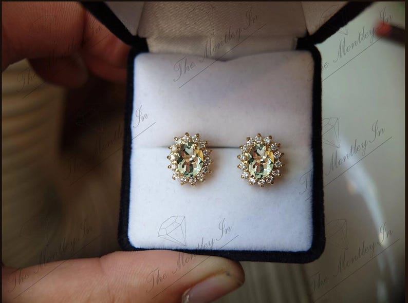 May include: A pair of gold earrings with oval-shaped green gemstones surrounded by a halo of smaller diamonds.