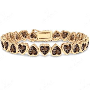 Puede incluir: Un brazalete de oro con un diseño en forma de corazón. El brazalete está adornado con piedras preciosas marrones en cada corazón.