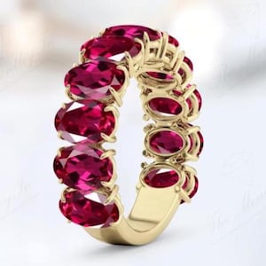 May include: A gold band ring with a row of oval-shaped ruby red gemstones.