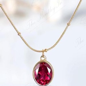 May include: A gold chain necklace with a round pendant featuring a large, red gemstone.