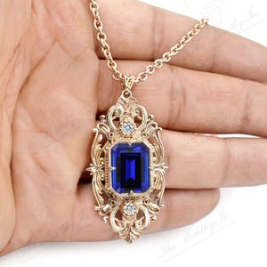 May include: A gold pendant necklace with a large blue gemstone set in a filigree frame. The pendant is ornate and features a detailed design.