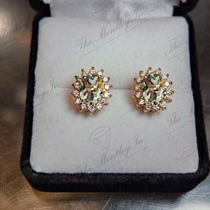 May include: A pair of gold earrings with oval-shaped green gemstones surrounded by a halo of smaller diamonds.