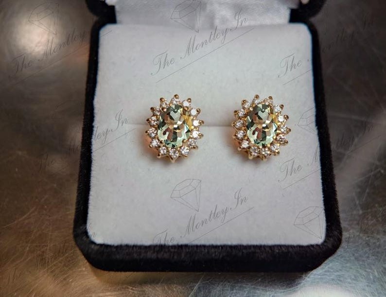 May include: A pair of gold earrings with oval-shaped green gemstones surrounded by a halo of smaller diamonds.